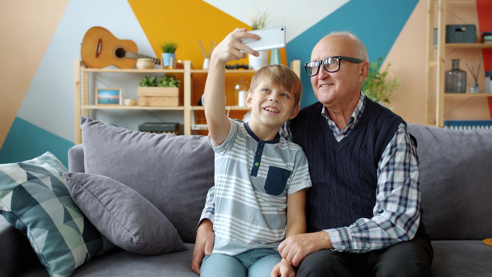 Grandfather and grandson taking a selfie on the couch.