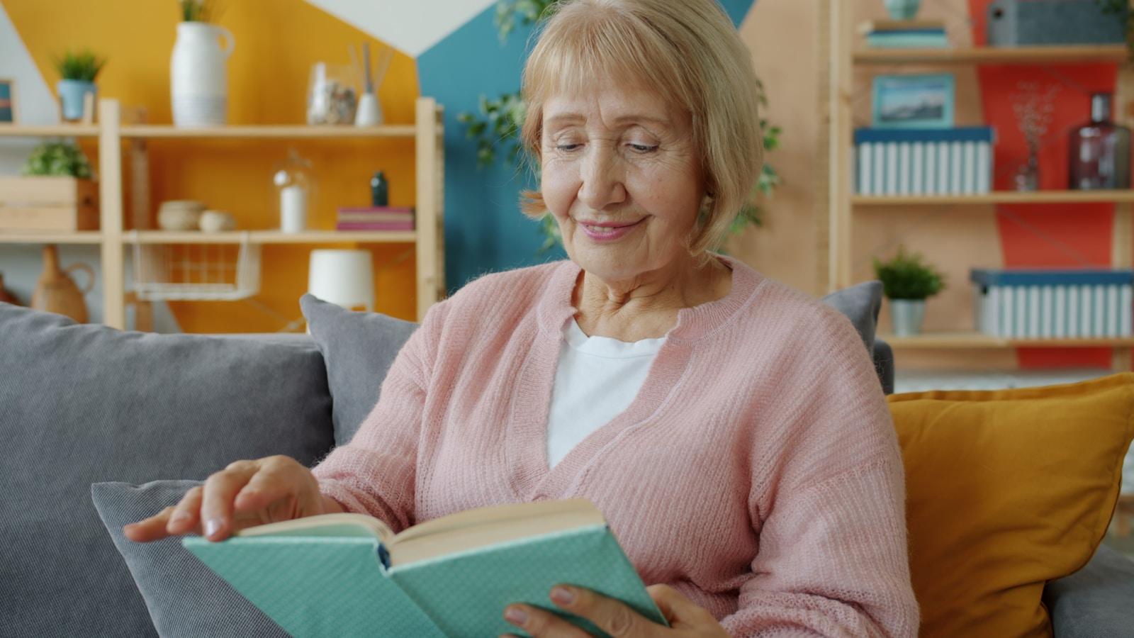 Elderly woman reading a book on a couch.
